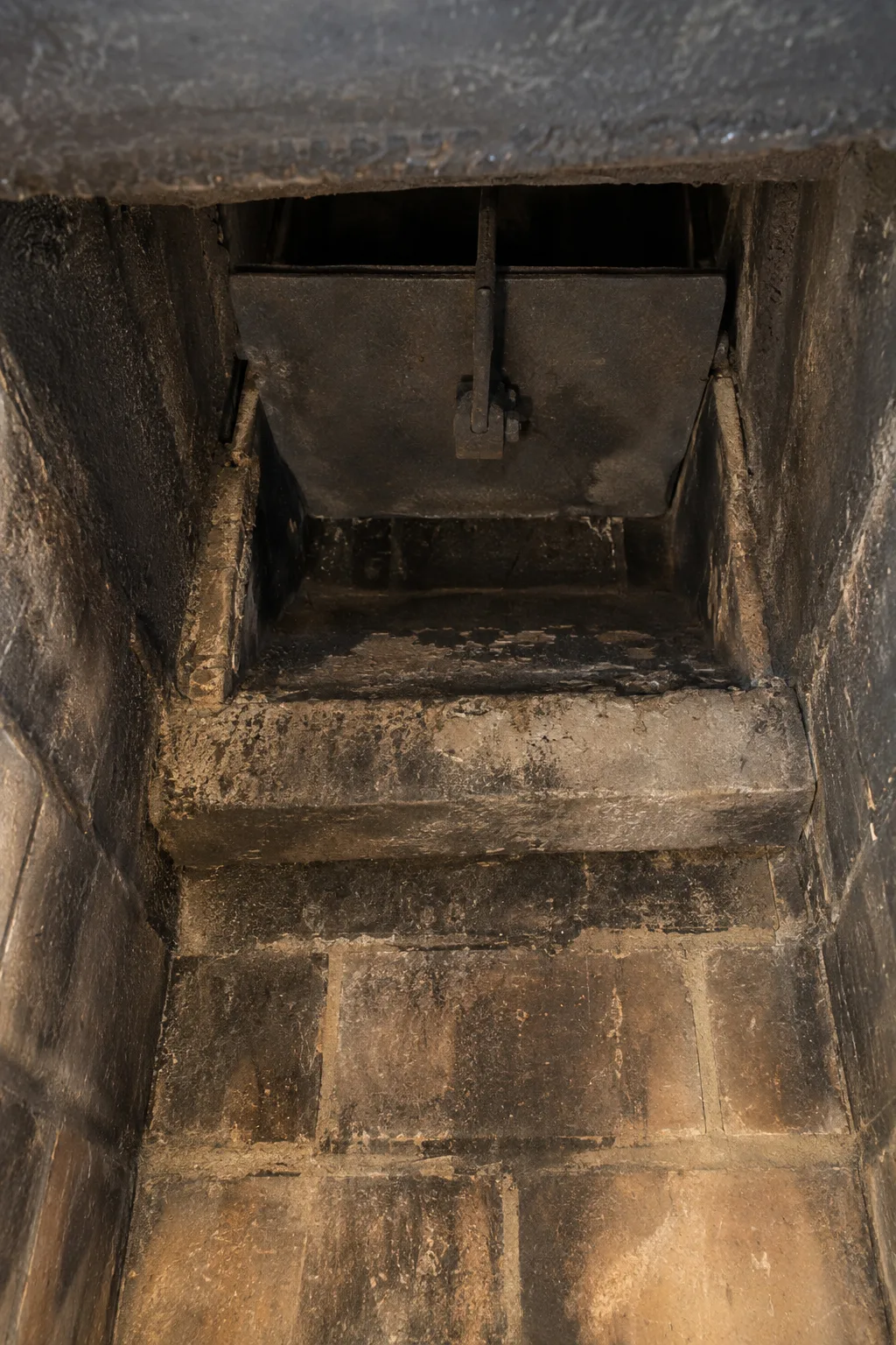 View looking up into a masonry firebox showing the smoke shelf, open cast-iron damper, and creosote-stained firebrick walls illuminated by a work light