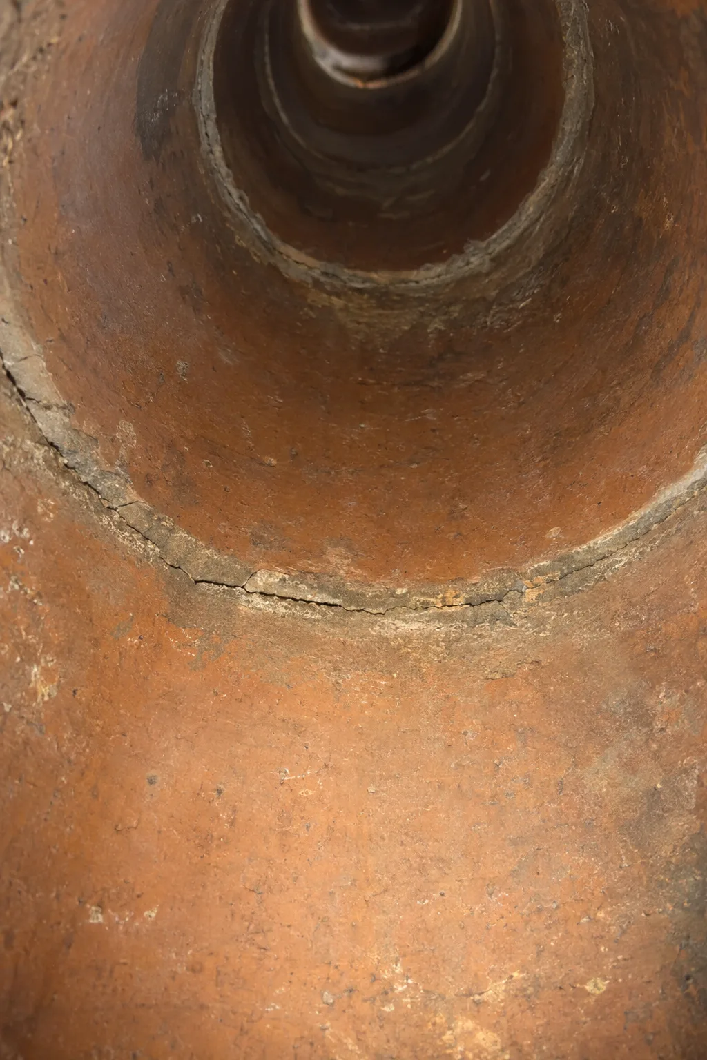 View up the inside of a round terra cotta chimney flue liner showing a cracked mortar joint and tile separation illuminated by a handheld work light, with the liner sections receding into darkness above
