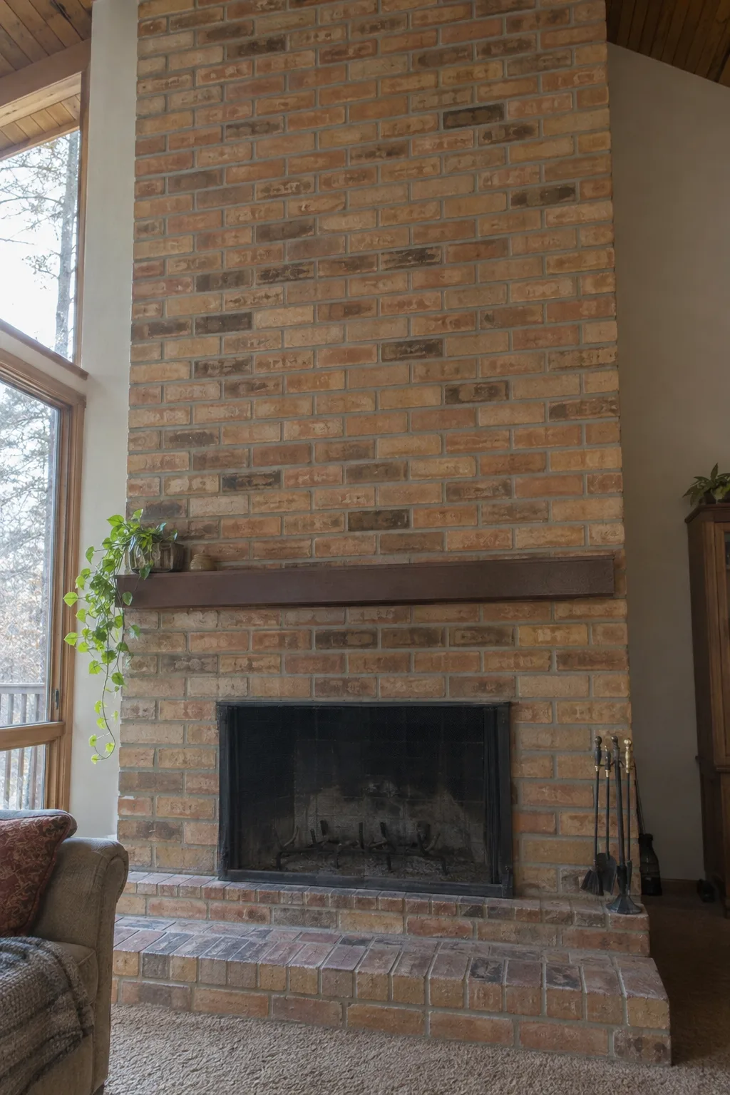 A floor-to-ceiling 1970s orange-tan brick fireplace surround with wide mortar joints and a flat low mantel shelf in a living room lit by warm afternoon sunlight