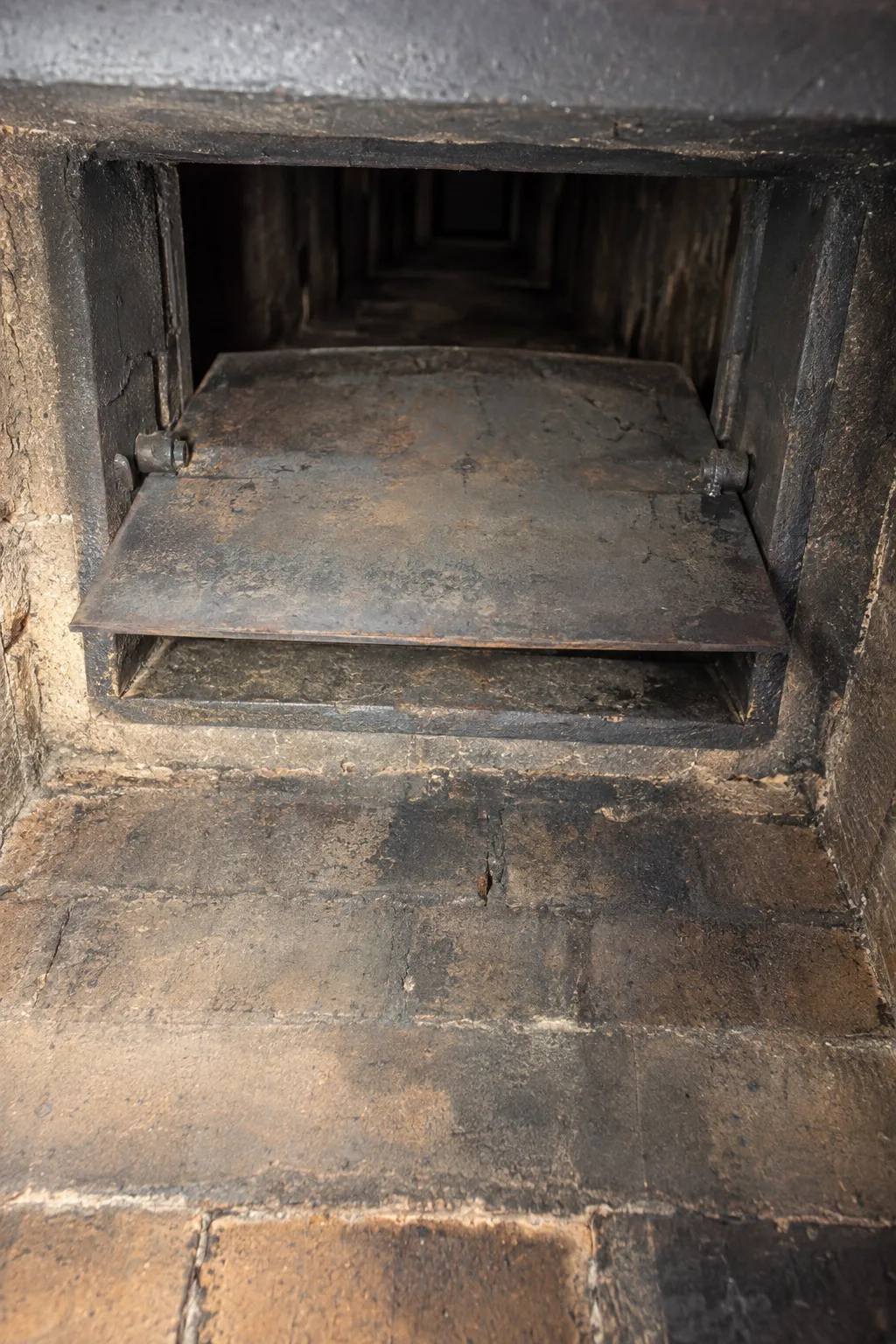 Close view inside a firebox looking up at a cast iron throat damper plate slightly open on its pivot pins, work light illuminating the frame