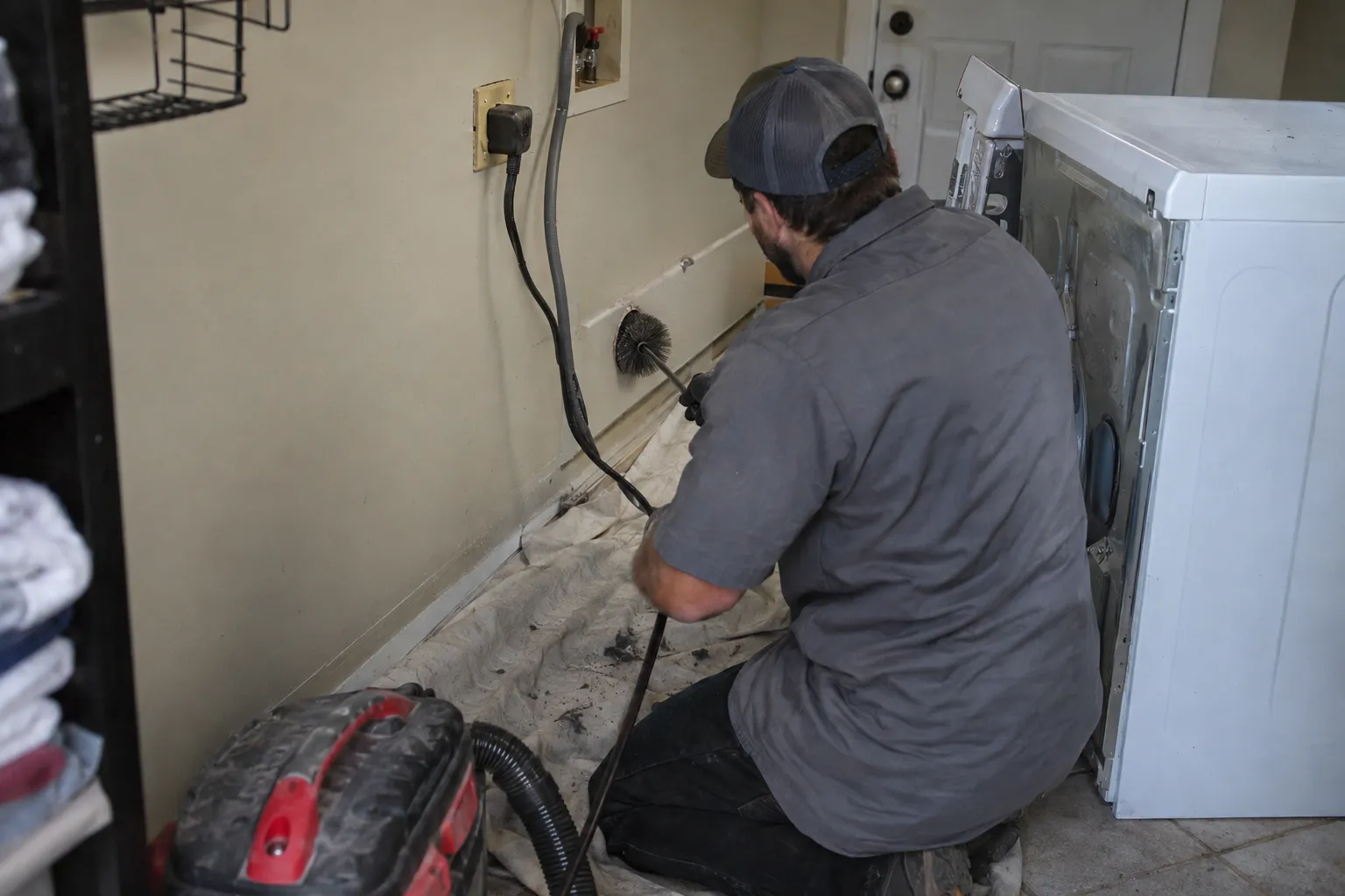 Technician running a rotary brush through a dryer vent in a laundry room